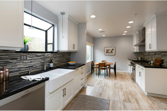 Skinny black and white tiles line walls under white kitchen cabinets and silver appliances.