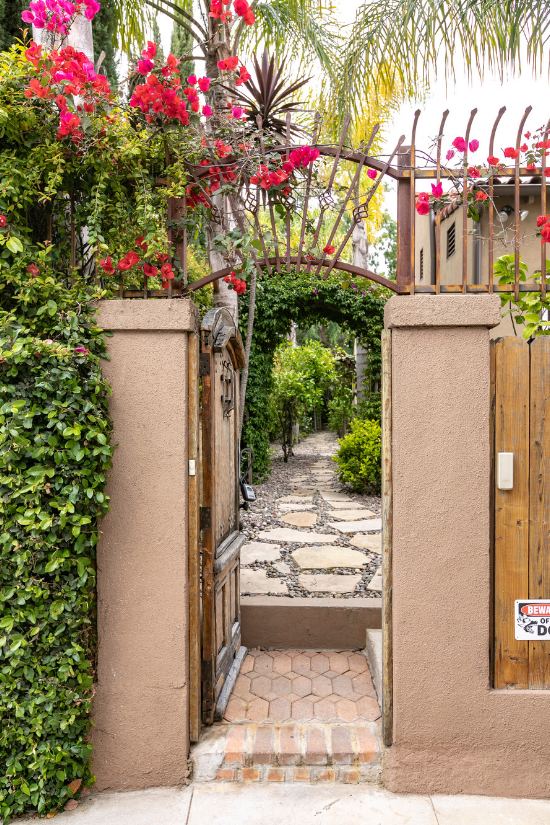 An antique wooden gate covered in bougainvilla opens up to a stone pathway.