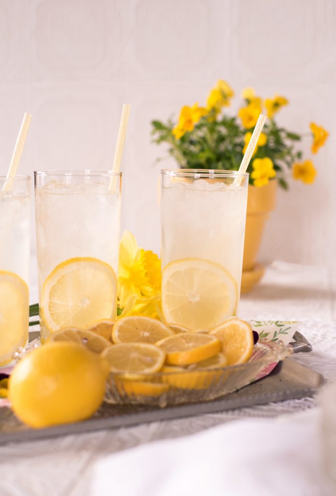 bright yellow lemons sit beside glasses of lemonade