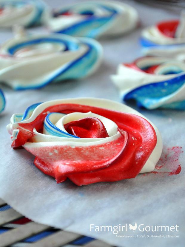 Airy red, white and blue striped meringues cool on parchment paper