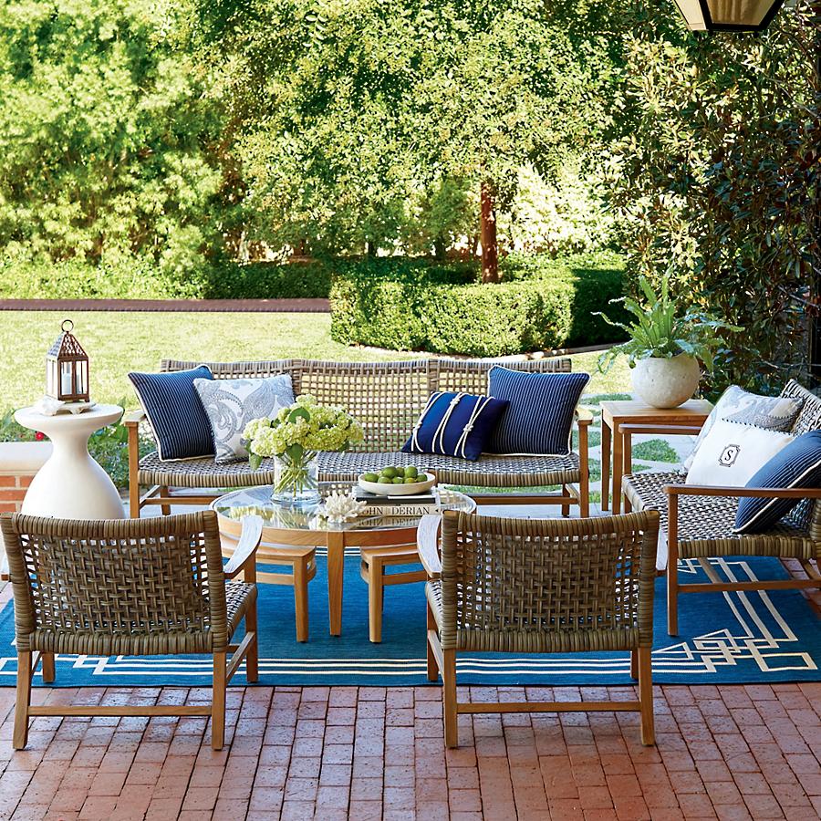 woven rattan sofa and chairs in a backyard brick patio on a blue rug
