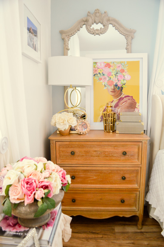 Wooden dresser topped with fresh flowers, gold accents, a large ornate mirror and a pop of colorful art. 