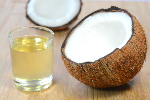 A glass of coconut oil next to an open fresh coconut