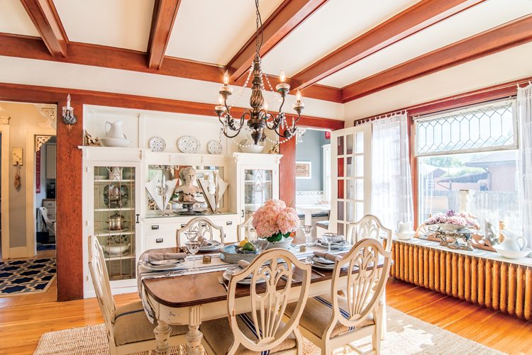 A found dining set re-painted and reupholstered by the owner, situated under exposed ceiling beams and an embellished chandelier. 