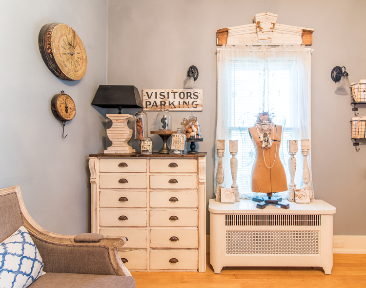 A guest room with a vintage white painted dresser and a wooden mannequin surrounded by candlesticks.