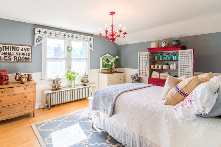 A bright red hutch pulls out red and blue accents in this farmhouse inspired bedroom. 