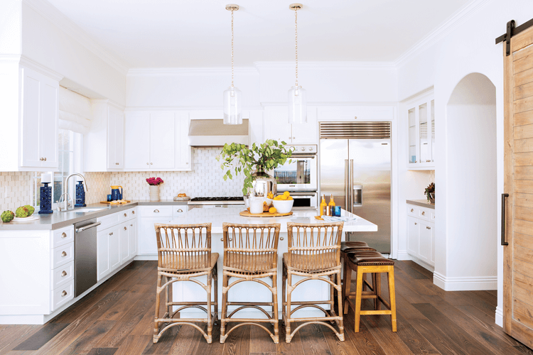 Rattan bar chairs lined up at a white marble topped island in an open concept kitchen. 