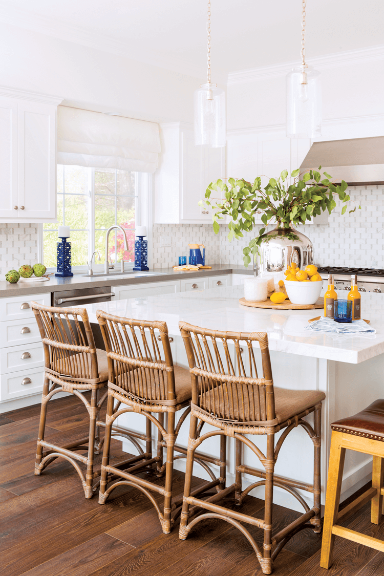 Rattan bar height chairs lined up at a marble topped island covered in fresh lemons in a bowl and lovely greenery for a pop of color.