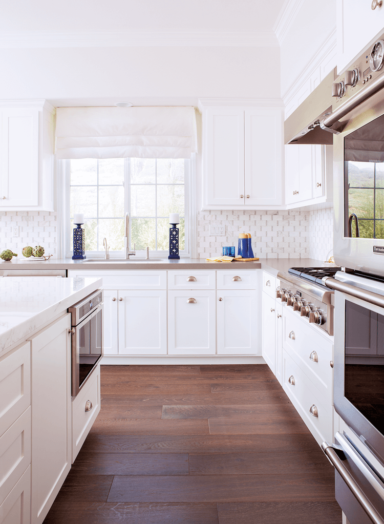 View down the galley in the heart of the kitchen. White custom cabinets and concrete countertops with stainless steel appliances. 