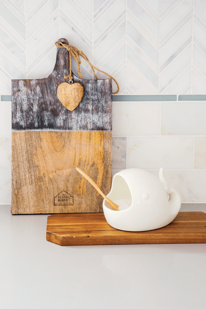 Kitchen countertops with glass liner and marble backsplash in a chevron pattern with cutting board and coastal inspired salt scooper. 