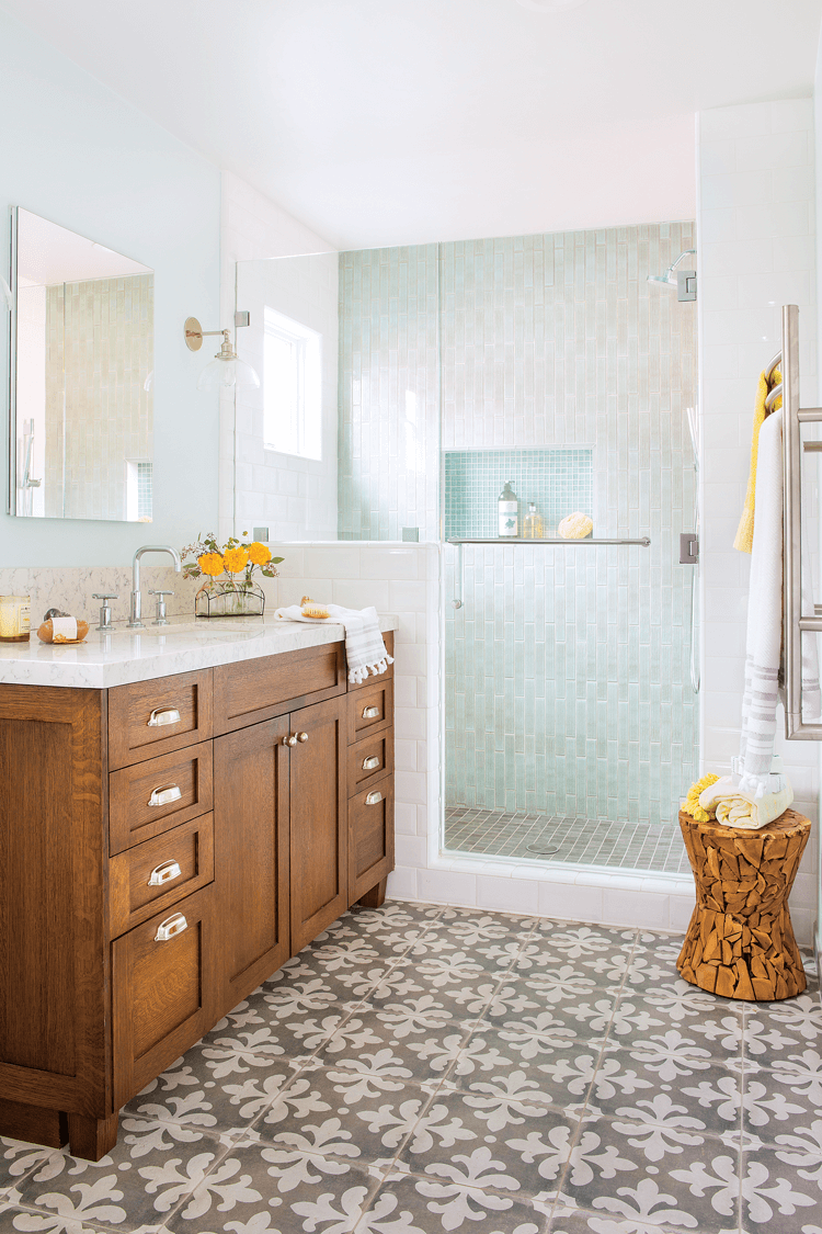 Wooden vanity in a bathroom, open concept tiled shower and faux-cement tiled floors with an intricate pattern. 