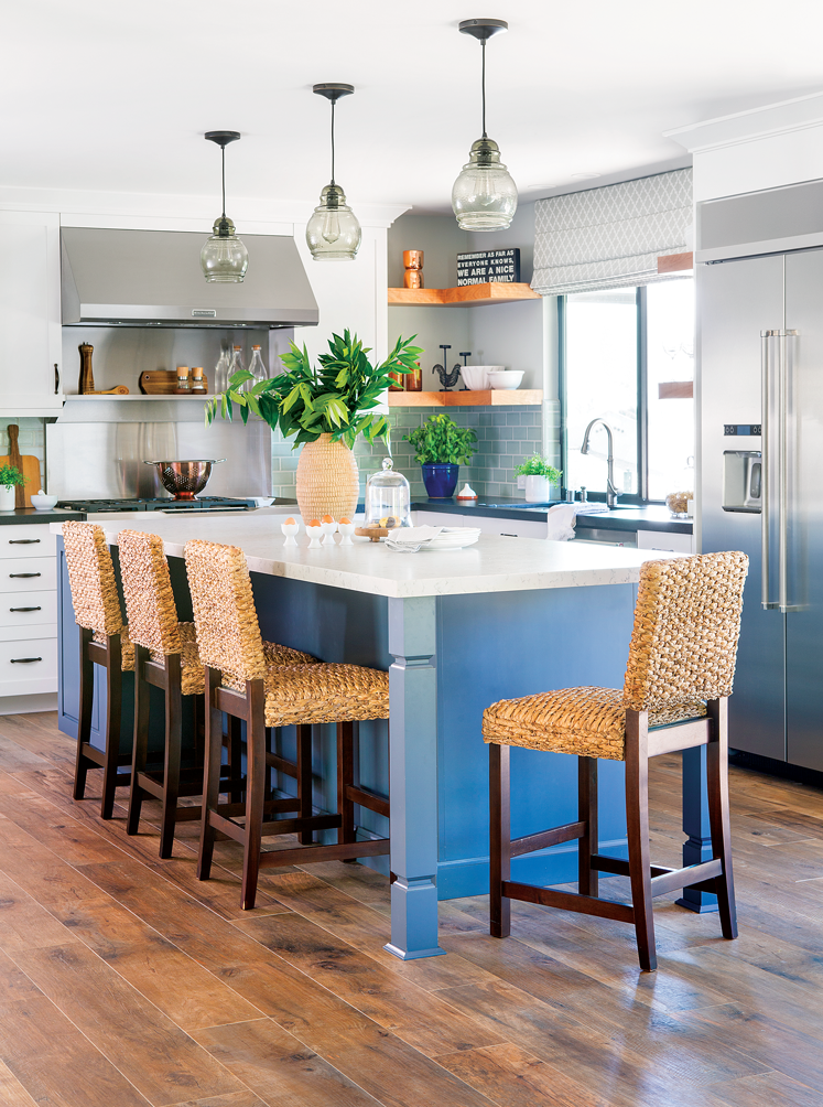 An open-concept kitchen with a large blue island with crisp white countertop and Routan bar height chairs.