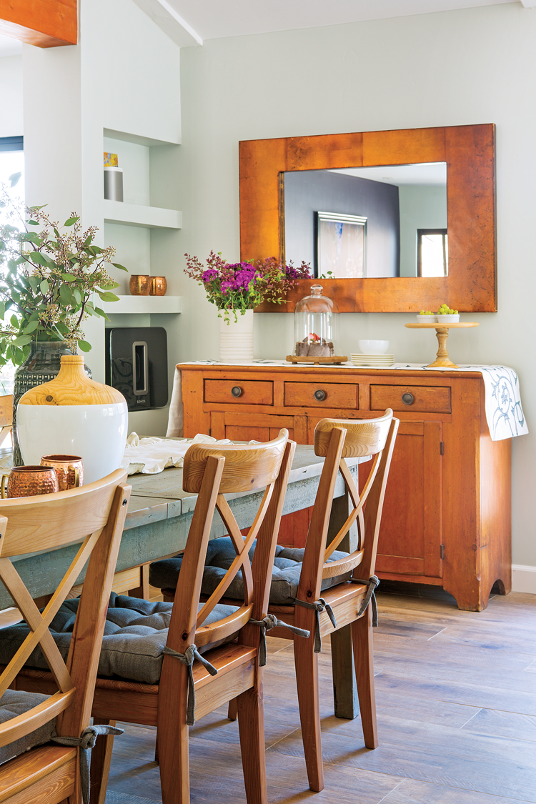 Rustic dining area with a warm wood toned sideboard beneath a rectangular mirror. 