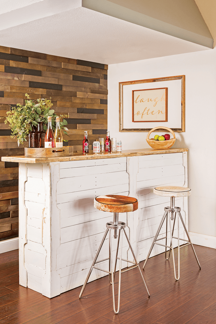 Modern hair-pinned leg barstools sitting at a rustic indoor bar. The bar is covered in white reclaimed shiplap and the accent wall behind it is also made of darker reclaimed wood pieces. 