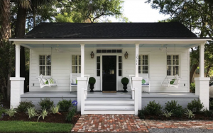 a white bungalow with a porch and black roof