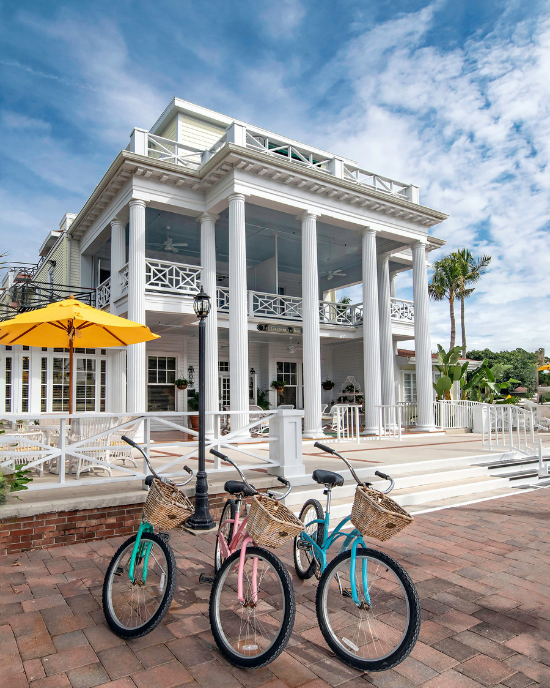 Three colorful beach cruiser bicycles with baskets parked in front of the Gasparilla Inn and Club.