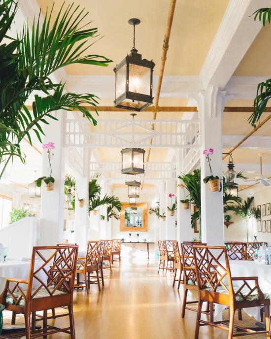 The Inn's Dining Room complete with high ceilings and hanging lanterns. Brown wooden latticed chairs and white linens.