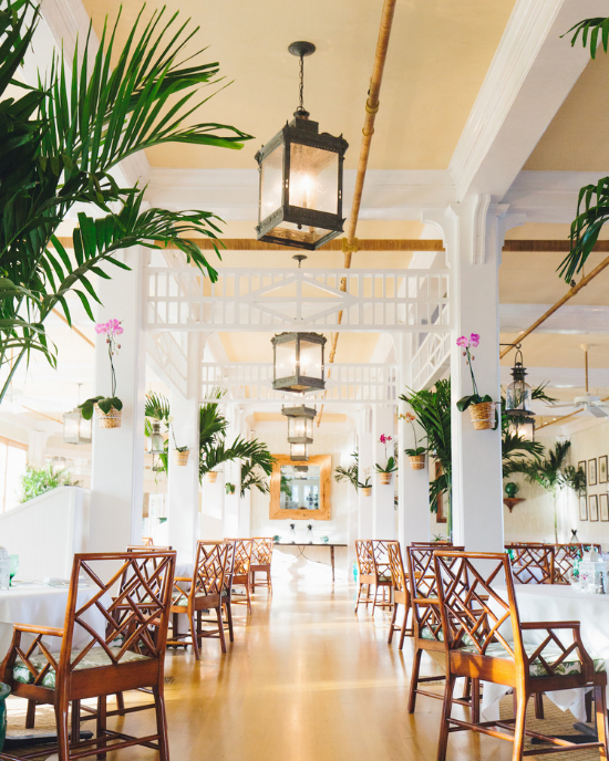 The Inn's Dining Room complete with high ceilings and hanging lanterns. Brown wooden latticed chairs and white linens. 