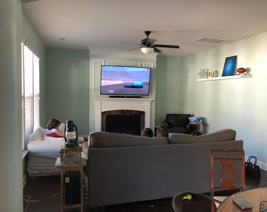 Before photo of a living room, tv above the fireplace and dark colored furniture. 