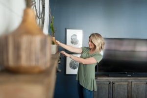 Blonde woman adjusting and placing items on a living room mantle.