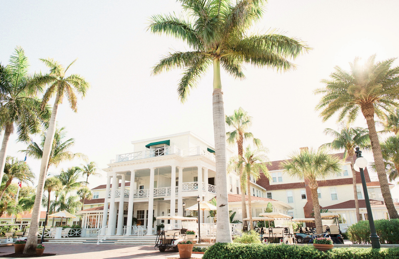 Front elevation of The Gasparilla Inn and Club in Florida. Stately columns on the front of the building and surrounded by palm trees.