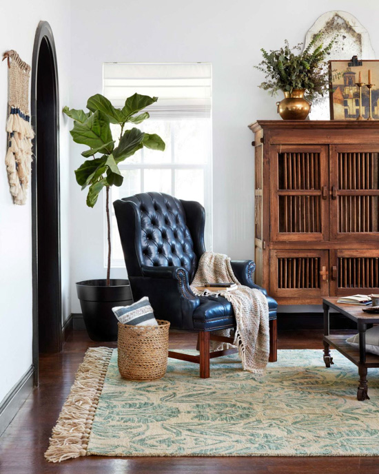 Black, tufted, leather wingback chair in front of a fiddle-leaf fig tree, showing off an aqua area rug from the new magnolia home collection. 