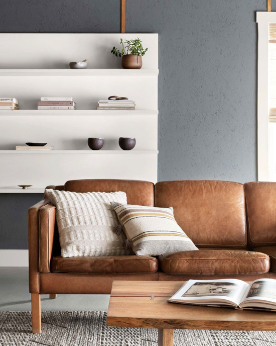 Leather brown couch with decorative pillows in front of modern white bookshelf.