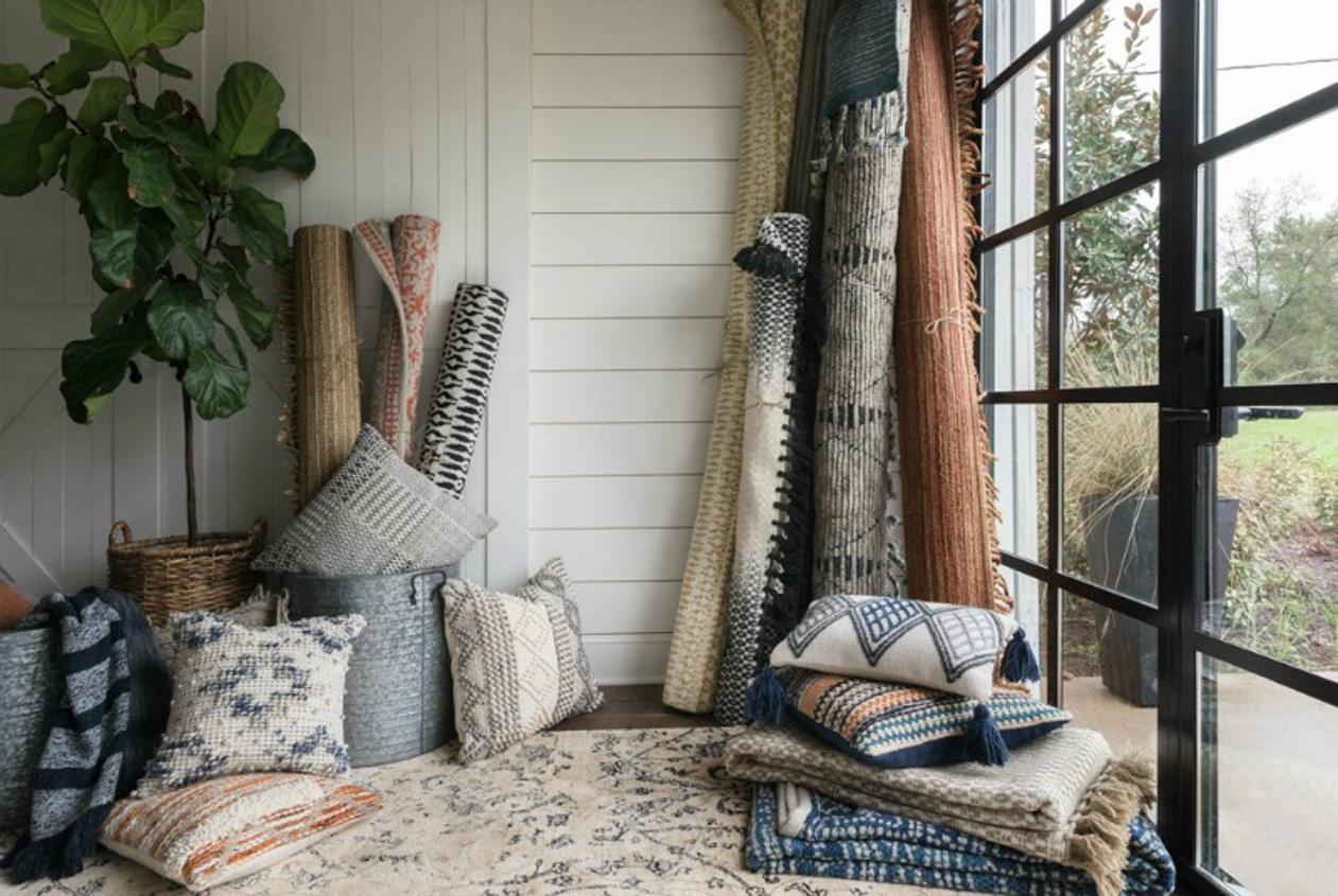 Textiles, rugs and pillows displayed near French doors with black metal framing.