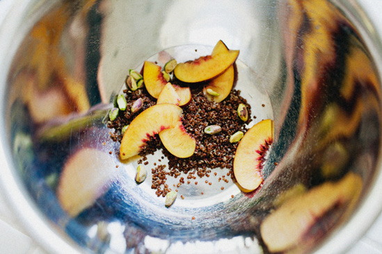 Looking inside a silver mixing bowl at nectarines, pistachios and quinoa. 