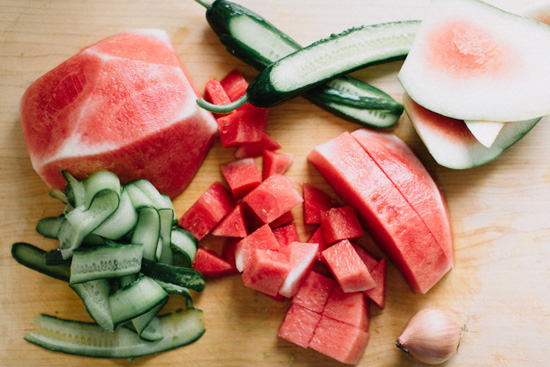 Cutting board covered in pieces of brightly colored watermelon and cucumber.