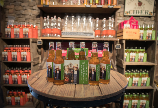 A rustic display of cider bottles in a few different varieties with a stone wall in the background.