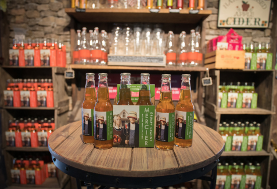 A rustic display of cider bottles in a few different varieties with a stone wall in the background. 