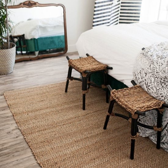 Handmade jute rug laid at the foot of the bed with two stools and across from a large mirror. 