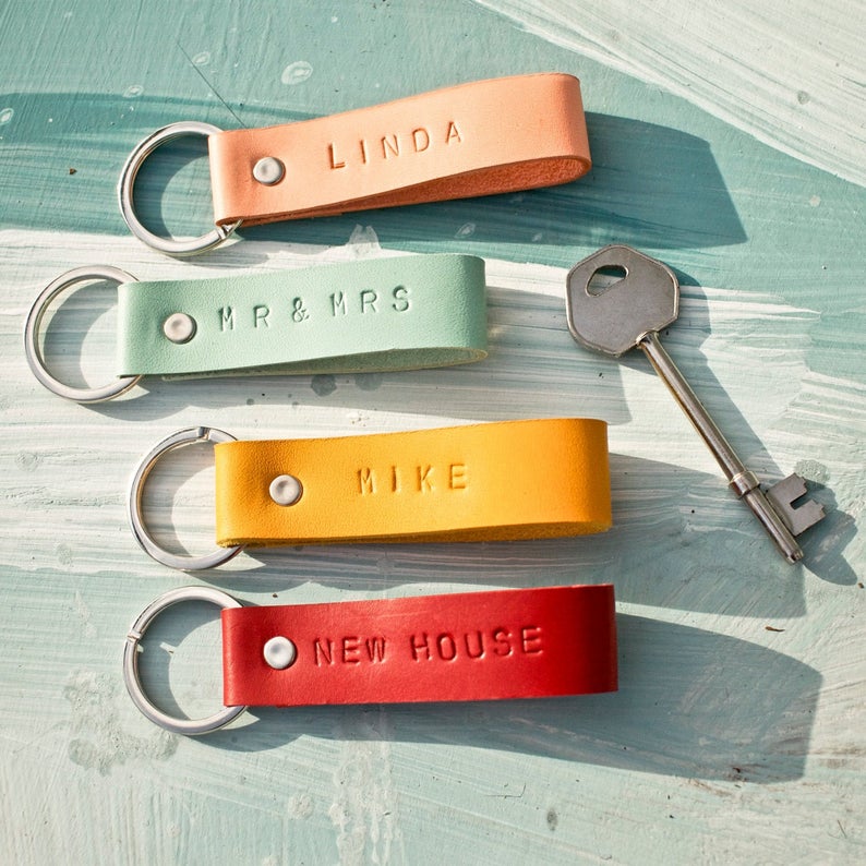 Four bright colored leather, monogrammed loops attached to a key ring arranged next to a silver key.