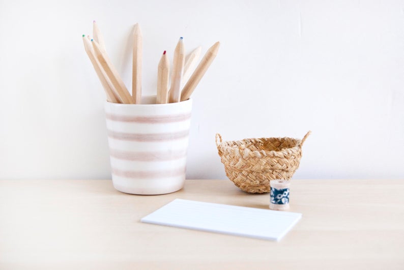 Light wood desk topped with a notepad, small basket, and a striped ceramic bowl filled with pencils. 