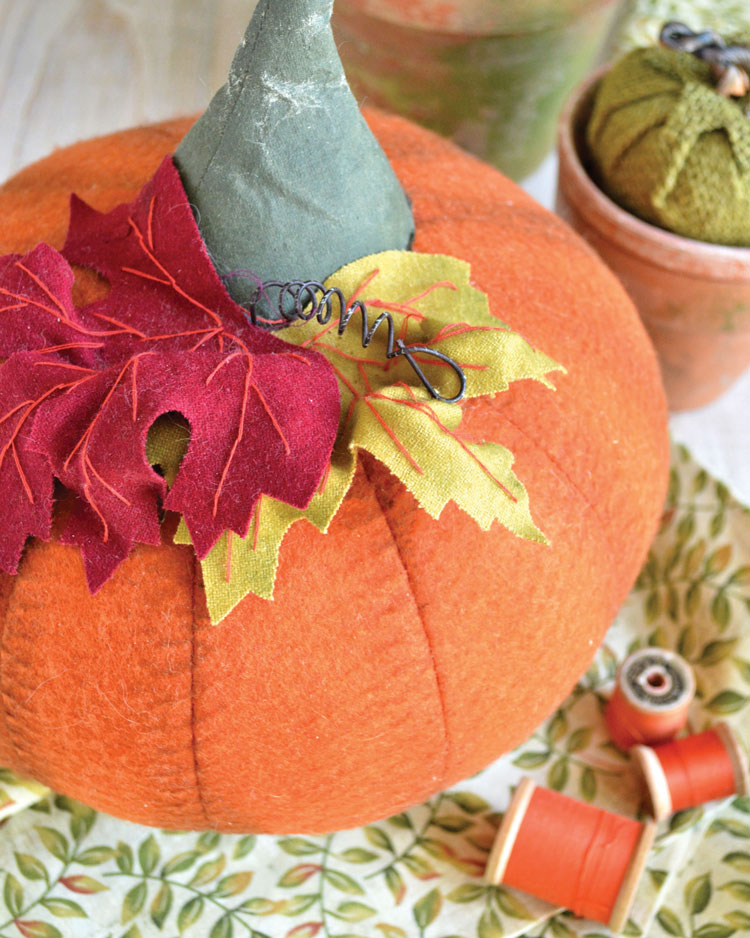 Felt fabric pumpkins surrounded by other crafted creations and spools of orange thread. 