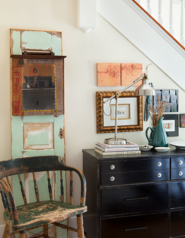 A small entryway near the stairs with repurposed old door as a piece of art near a vintage desk and chair.