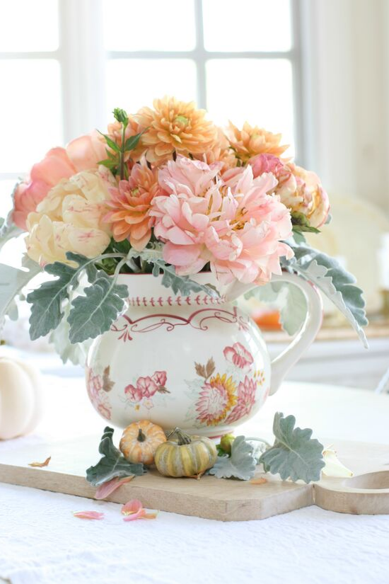 A hand-painted pitcher sitting on a wooden cutting board and filled with pink peonies and sherbet colored dahlias.