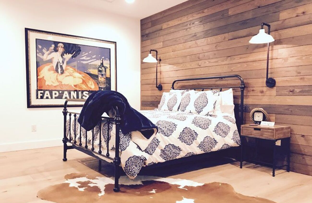 Cow hide rug under dark metal framed bed placed in front of an accent wall of reclaimed wood panels.