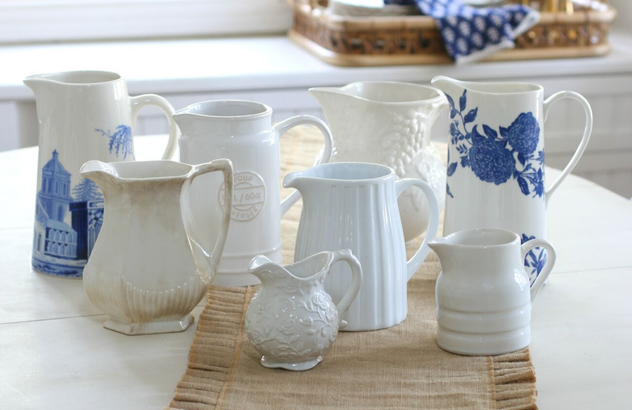 A collection of pitchers in varying shades and shapes arranged on a dining table with a linen runner.