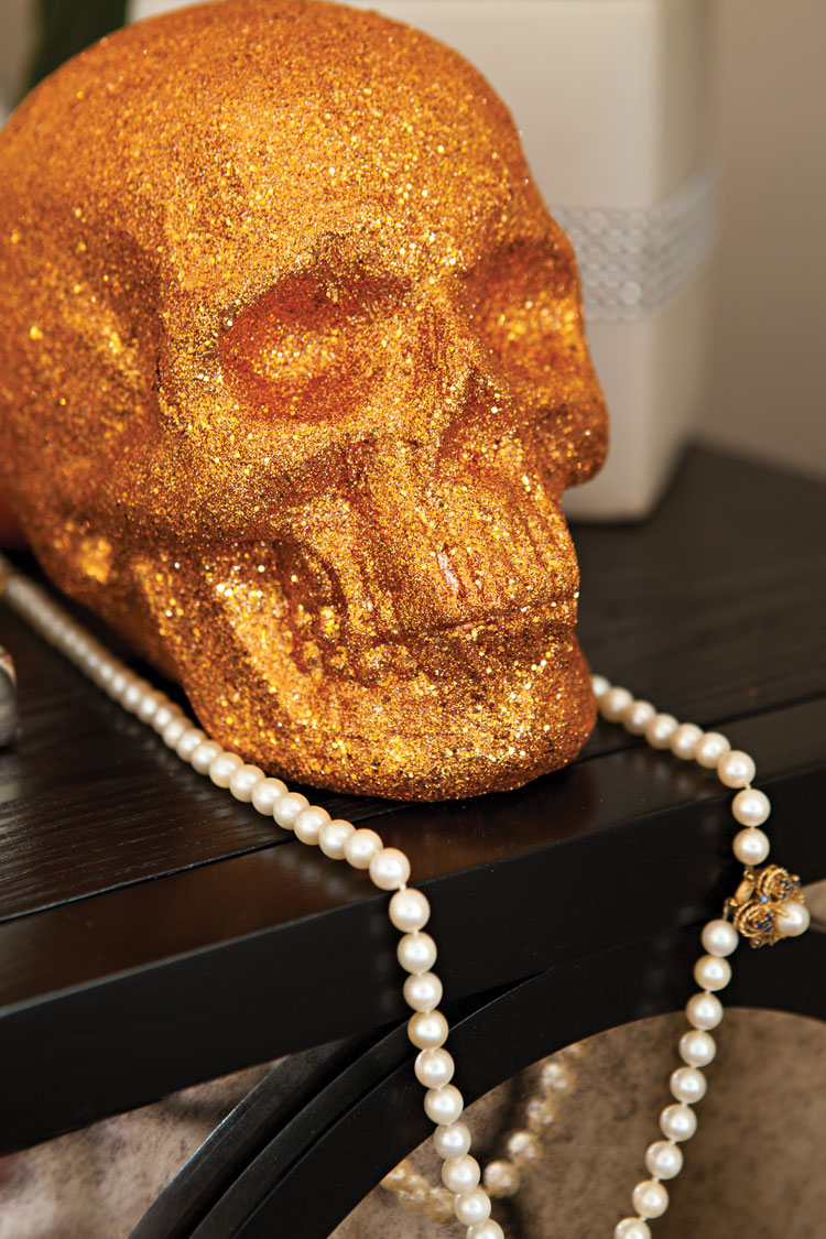 Bright orange skull covered in glitter and a strand of vintage pearls adorn a table as party decor. 