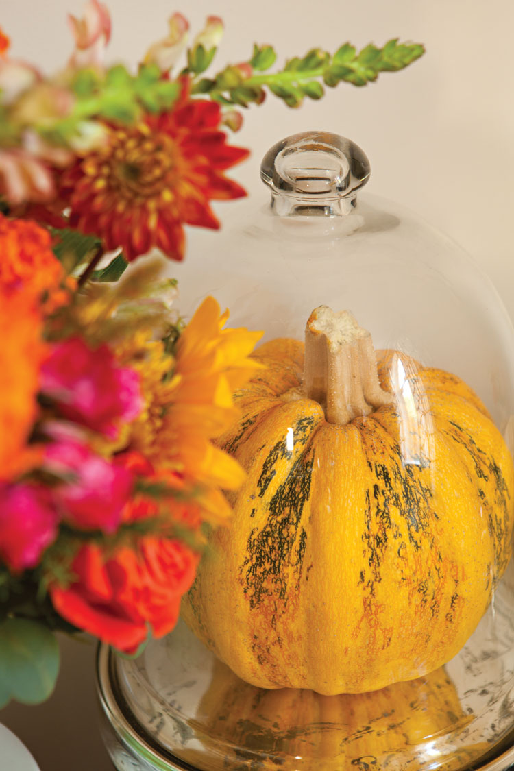 Bright floral centerpiece next to a pumpkin under a glass cloche. 