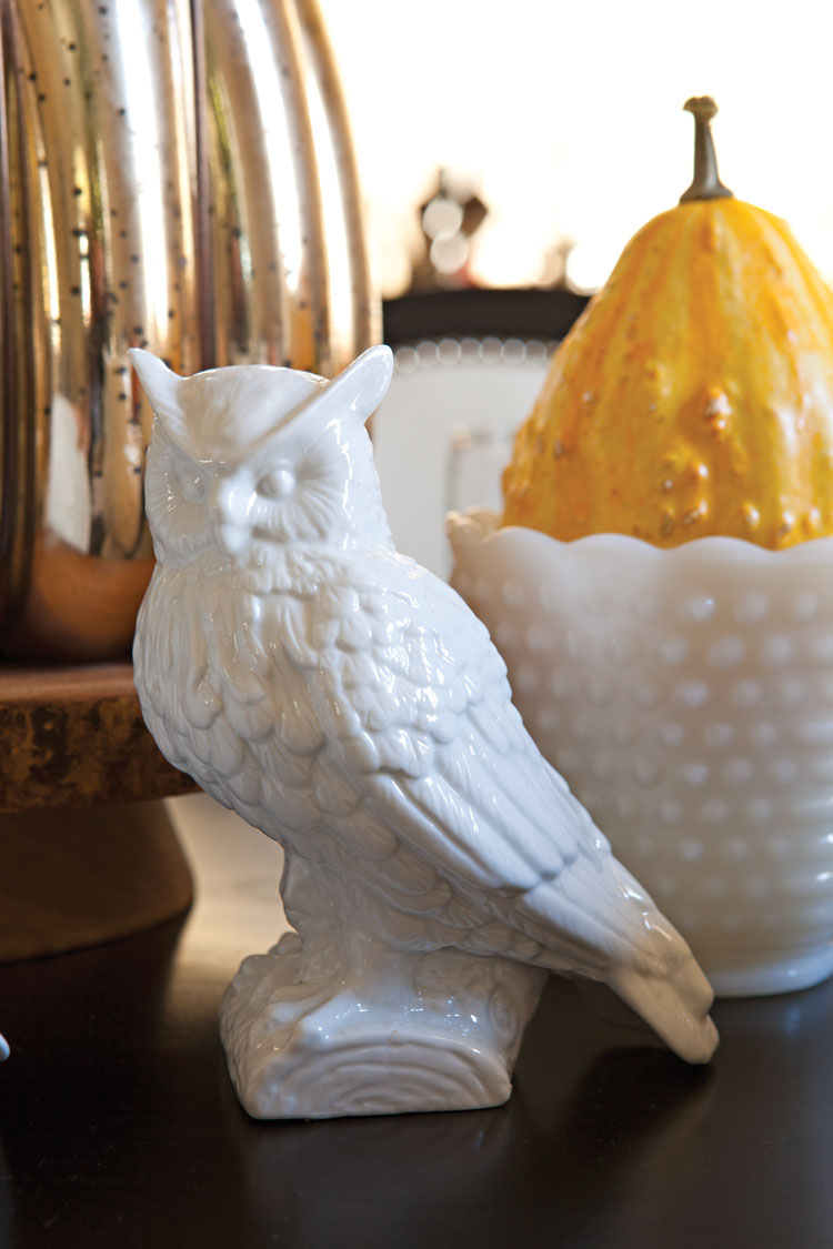 Centerpiece made up of a white porcelain owl figurine, a milk glass vase filled with a gourd and a gold metallic pumpkin.