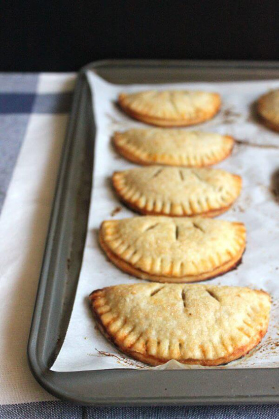 A baking tray lined with five small apple hand pies arranged on parchment paper. 