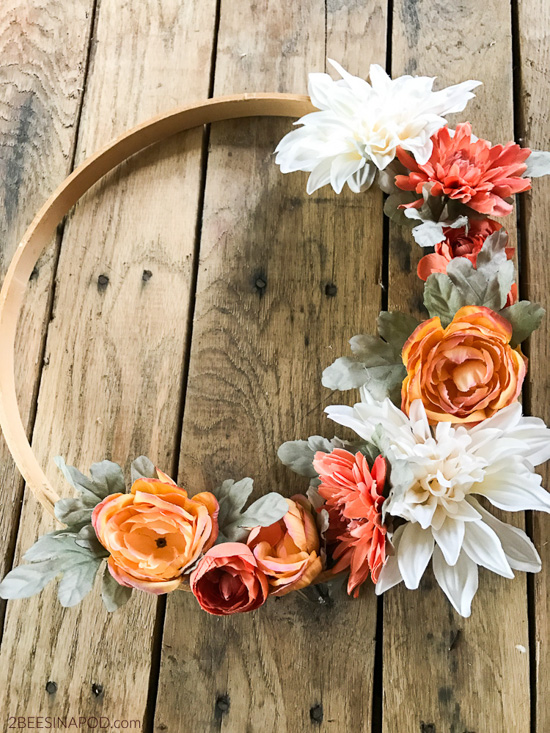 Embroidery loop decorated with fall colored florals and laying on a wooden table. 