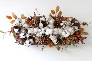 Dough bowl centerpiece on a white backdrop filled with natural autumnal decor.