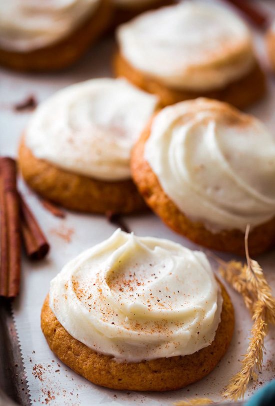 Pumpkin cookies on a cookie sheet and topped with cream cheese frosting. 