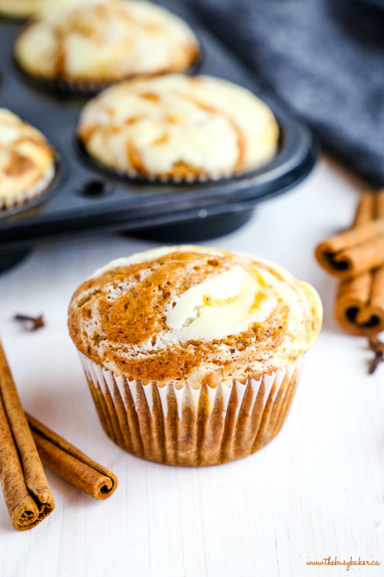 Pumpkin cream cheese muffins arranged in a muffin tin and cinnamon sticks as decoration. 