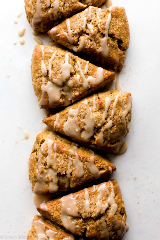 Pumpkin scones in a triangle shape arranged in a long row and topped with drizzle. 