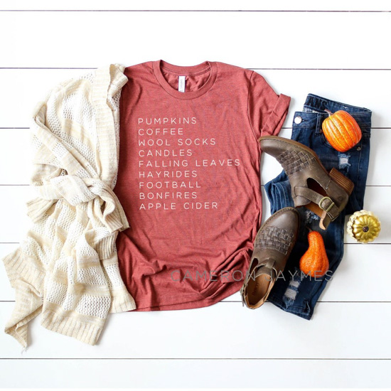 Fall outfit flat-lay. Cream sweater, t-shirt with a list of fall favorite things, dark denim jeans, brown booties and Halloween gourds plaid around them.